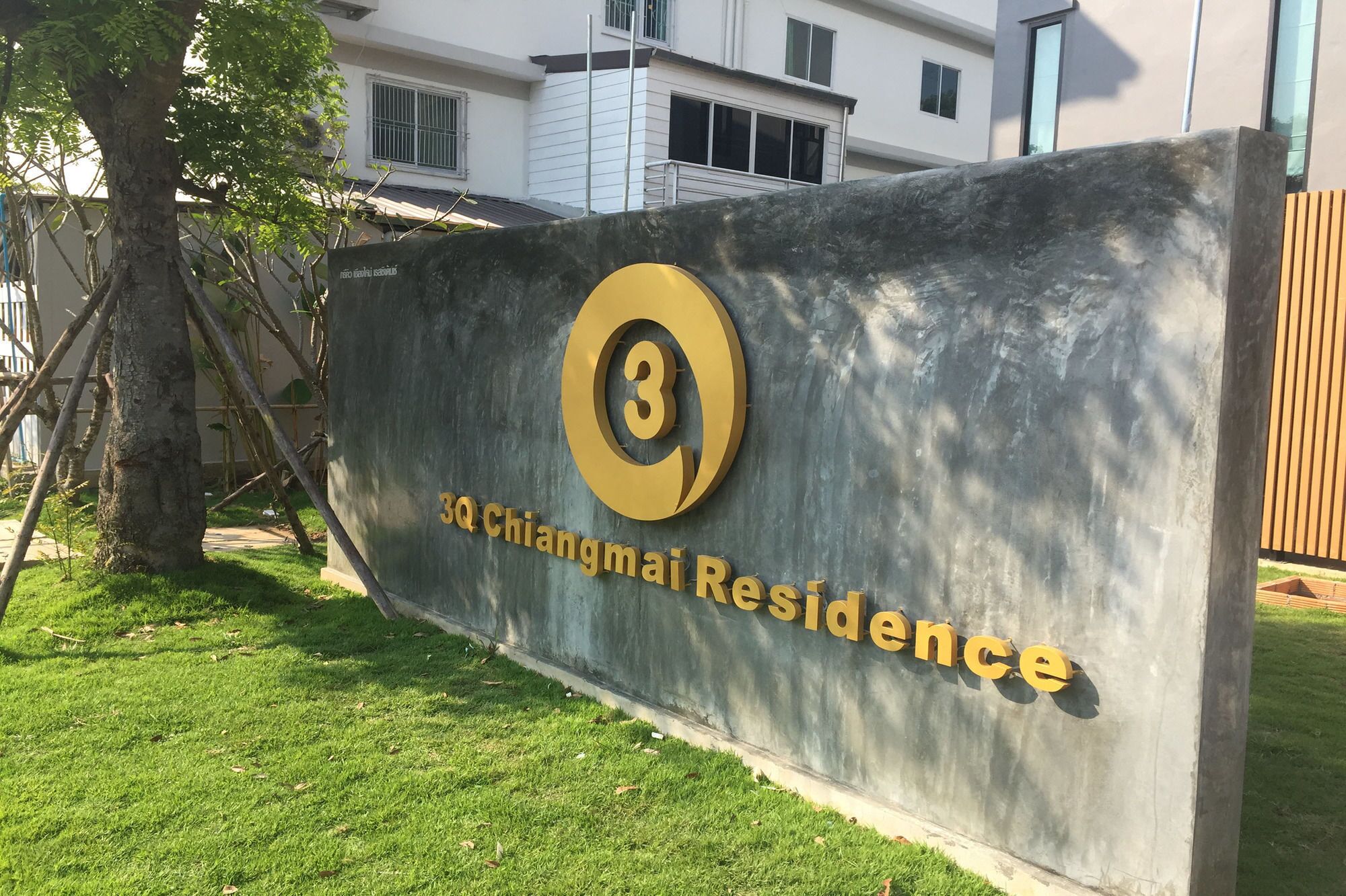 Señal de 3Q Chiangmai Residence con un gran número '3' y el nombre '3Q Chiangmai Residence' en letras doradas sobre un fondo gris.