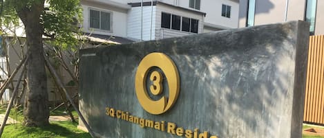 A sign for 3Q Chiangmai Residence with a large number '3' and the name '3Q Chiangmai Residence' in gold lettering on a grey background.