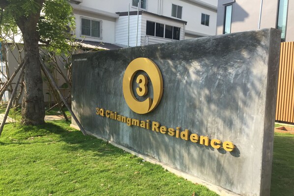 A sign for 3Q Chiangmai Residence with a large number '3' and the name '3Q Chiangmai Residence' in gold lettering on a grey background.
