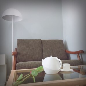 A room with a sofa, a table with a teapot and cup, and a floor lamp.