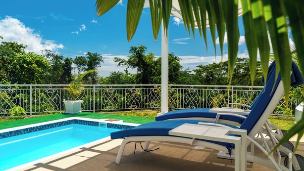 Piscina com espreguiçadeiras, cercada por uma vedação e vegetação.