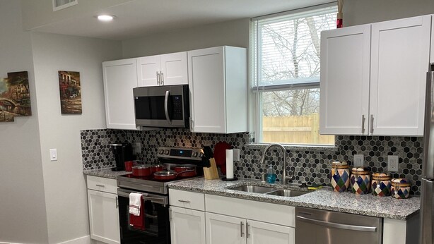A modern kitchen with white cabinets, a stainless steel refrigerator, a microwave, and a dishwasher.