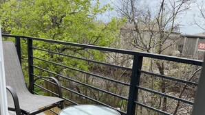 A balcony with a stone floor, metal railing, and two chairs with a small glass table.