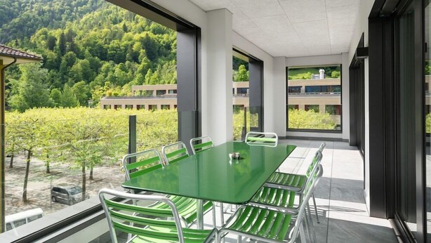 A modern meeting room with a glass table and green chairs, large windows offering a view of a forested hillside. - Swiss Hotel Apartments Interlaken (Interlaken)
