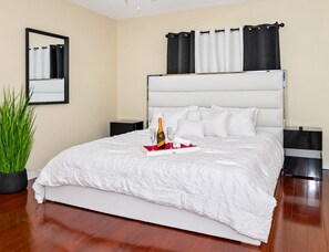 A hotel room with a large bed, a bedside table, a nightstand, a potted plant, and a mirror on the wall. - Spacious & Amazing Home w/ Big Pool and Patio (Brandon)