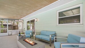 A modern outdoor living area with a fire pit, blue seating, and a large window with blinds. - Spacious & Amazing Home w/ Big Pool and Patio (Brandon)