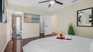 A bedroom with a bed, a ceiling fan, a painting, a plant, and a bottle of champagne on the bed. - Spacious & Amazing Home w/ Big Pool and Patio (Brandon)