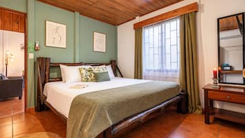 A hotel room with a wooden bed, a bedside table, a mirror, and a window with curtains.