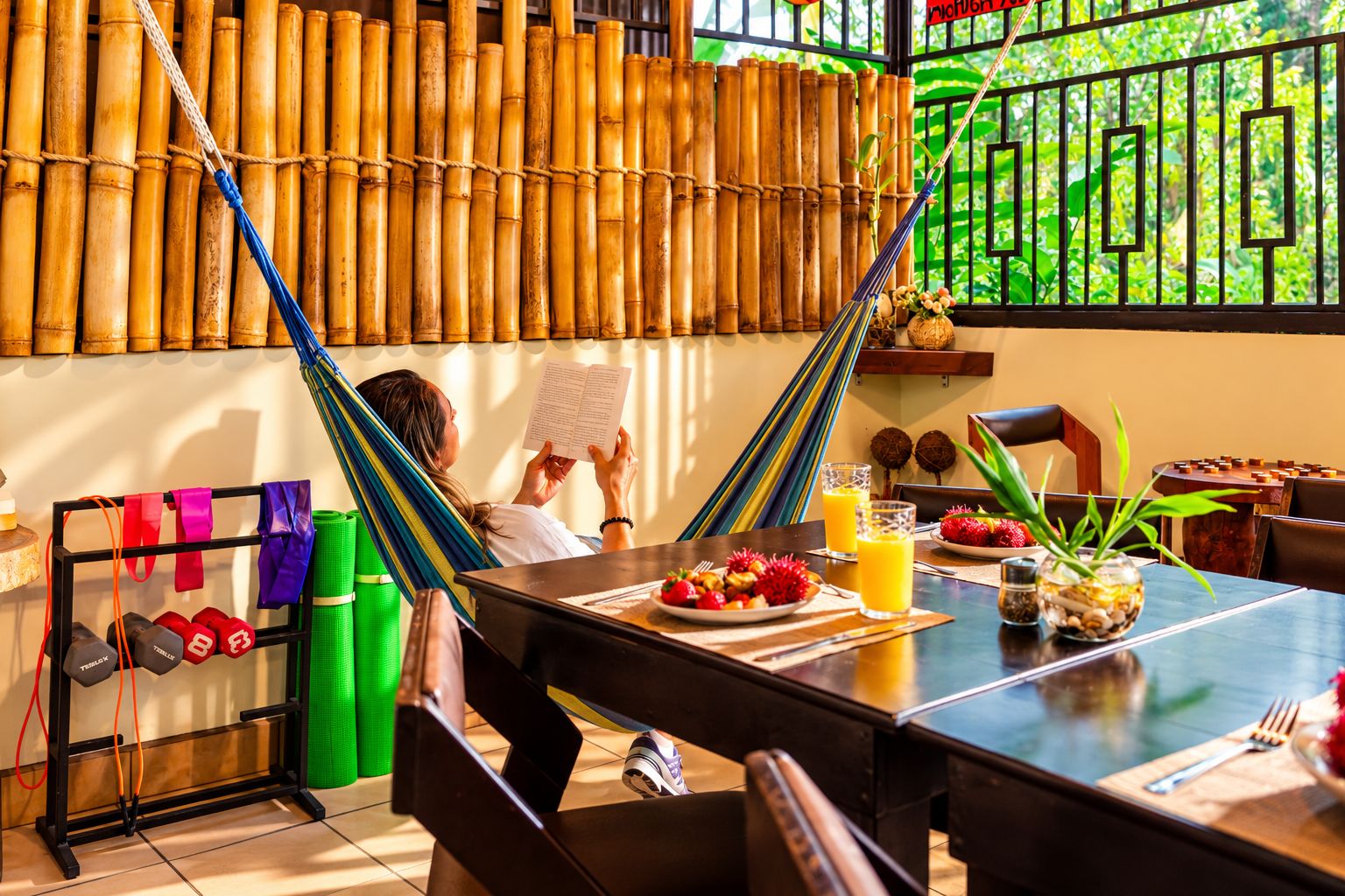 A room with a bamboo wall, a dining table with fruit and drinks, and exercise equipment.