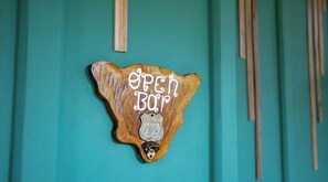 Ein hölzernes Schild mit der Aufschrift 'OPEN BAR' und 'ROUTE 66' an einer türkisblauen Wand.