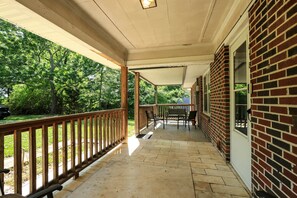 A covered porch with a brick wall, wooden railing, and a bench.