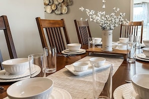 A dining table set with white bowls, plates, and glasses, surrounded by wooden chairs.