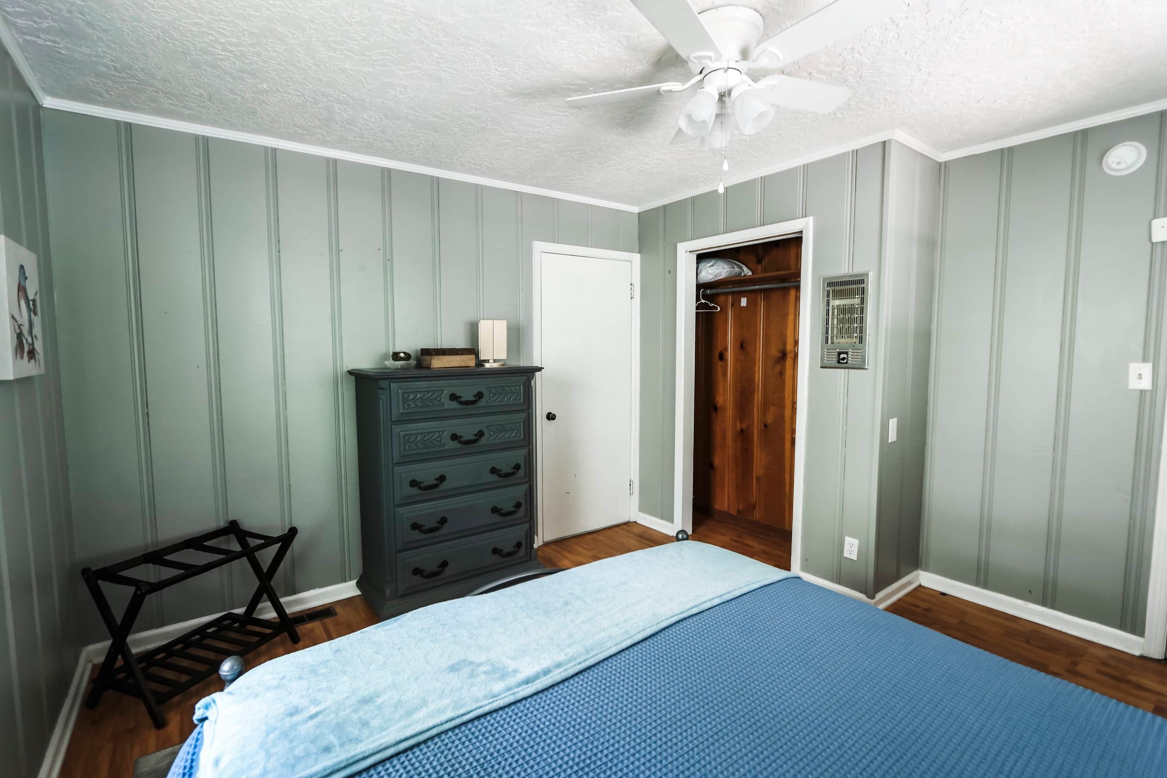 A bedroom with a bed, a dresser, a closet, and a ceiling fan.