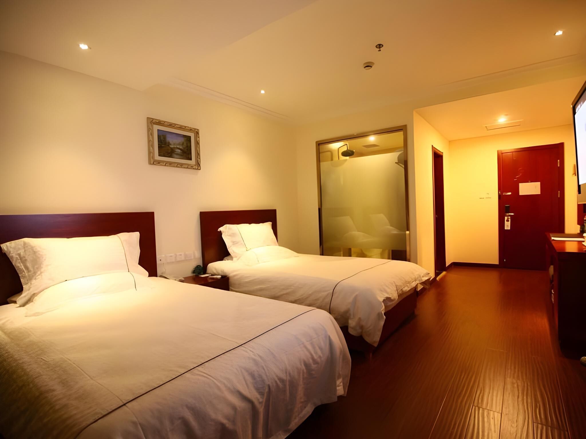 Habitación de hotel con dos camas, un cuadro en la pared, una puerta con espejo y suelo de madera.