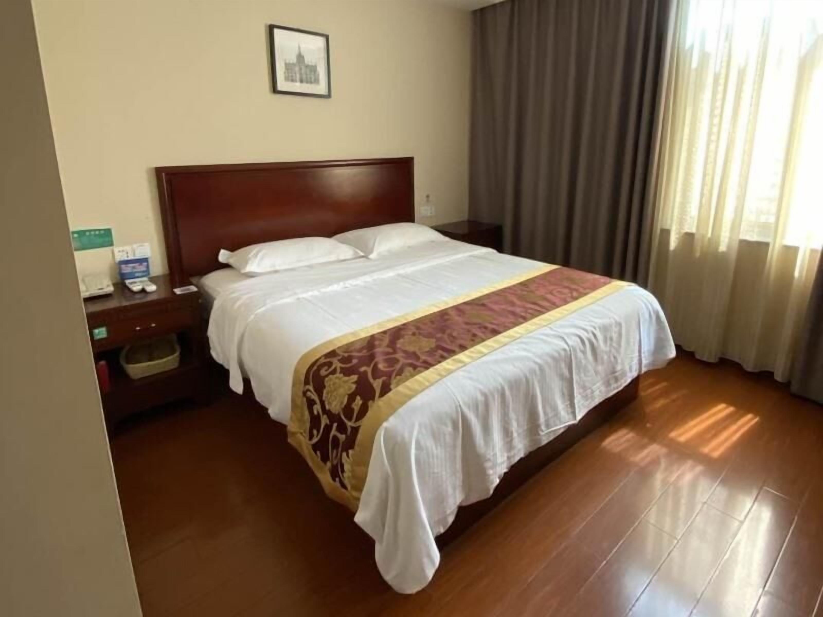 Une chambre d’hôtel avec un lit en bois, une table de chevet, un tableau encadré au mur et une fenêtre avec des rideaux.