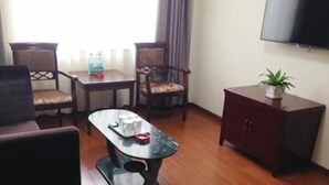 Ein Hotelzimmer mit Holzboden, einem kleinen Tisch mit Tablett, zwei Stühlen, einem Schrank und einem Fernseher an der Wand.