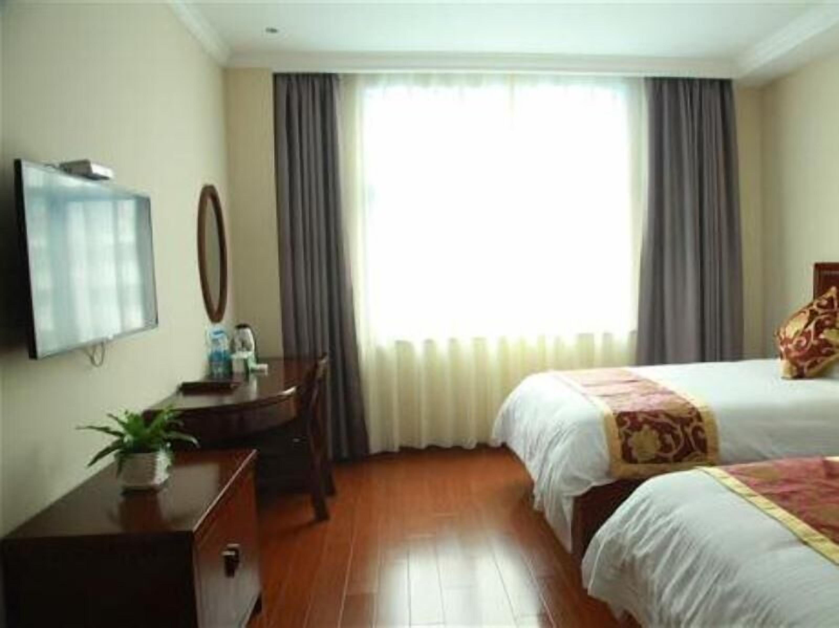 A hotel room with a bed, a desk with a chair, a television, and a window with curtains.