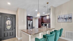 A modern kitchen with granite countertops, stainless steel appliances, and teal bar stools. - Casa De Paradiso - Modern yet comfy home at the center of it all! (Kissimmee)
