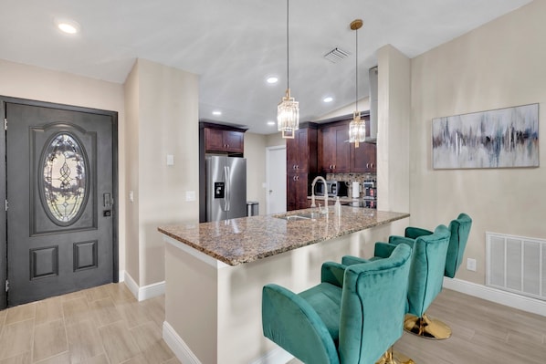 A modern kitchen with granite countertops, stainless steel appliances, and teal bar stools. - Casa De Paradiso - Modern yet comfy home at the center of it all! (Kissimmee)