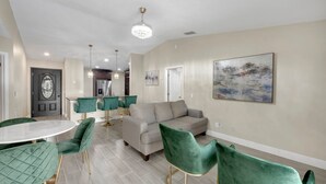 A modern living room with a grey sofa, green velvet chairs, a round dining table, and a chandelier. - Casa De Paradiso - Modern yet comfy home at the center of it all! (Kissimmee)
