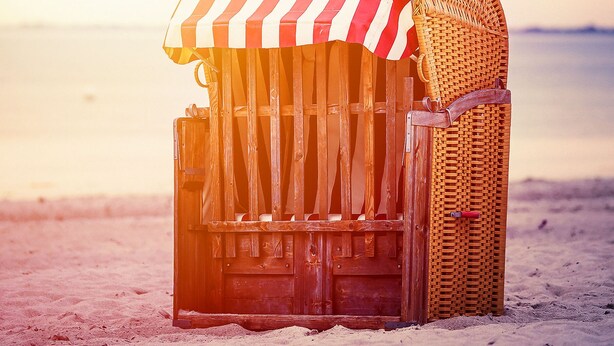 Een houten constructie aan het strand met een gestreepte luifel, waarschijnlijk een strandhut of kiosk, gelegen op een zandstrand met een rustige zee op de achtergrond.