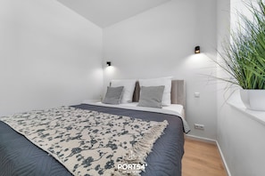 A modern bedroom with a bed, bedside lamps, a potted plant, and a patterned rug.