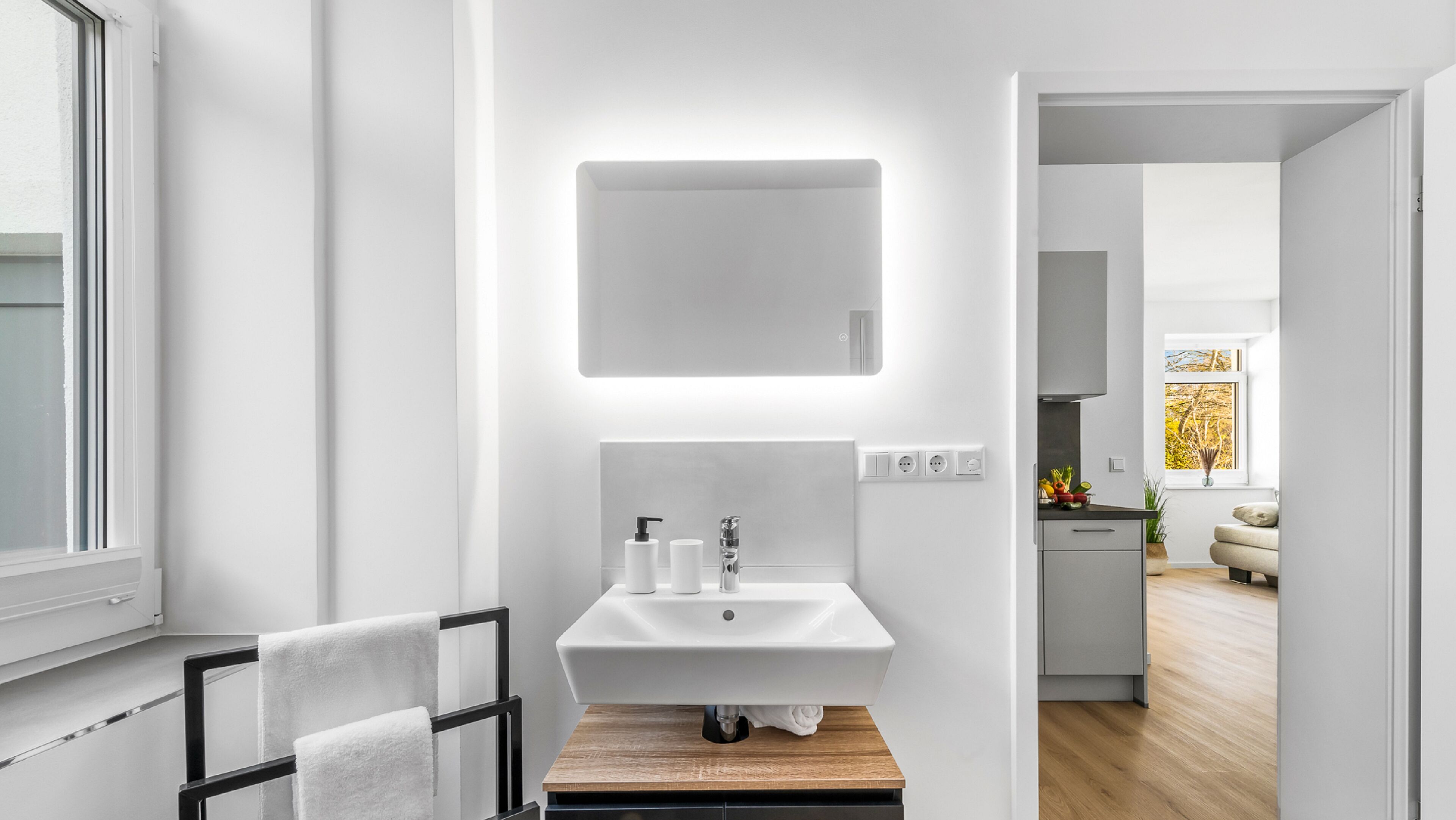 Un baño moderno con un lavabo blanco, un espejo y un perchero para toallas.