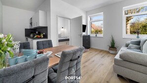 A modern kitchen with white cabinets, a wooden dining table, and a grey sofa. - Strandläufer - Shower, TV, Terrace, Garden Furniture, Grill, Parking Space (Gelting)