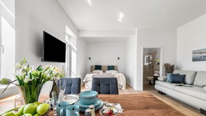 En moderne stue med sofa, spisebord dækket med tallerkener, glas og en vase med blomster.