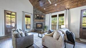 A spacious living room with a fireplace, wooden ceiling, and large windows.