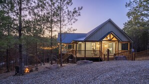 A cabin with a covered deck, a fire pit, and a staircase leading to the main entrance.
