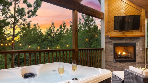 A hot tub with two glasses of champagne, a fireplace, and a TV on a wooden wall.