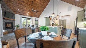 A spacious living area with a fireplace, dining table set for four, and a kitchen with modern appliances.