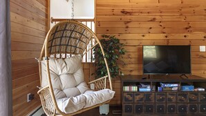 Una habitación acogedora con una silla colgante de mimbre, un televisor de pantalla plana y un mueble de madera con juegos.