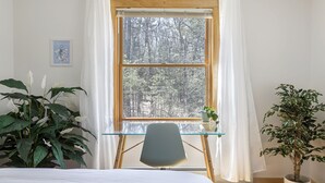 Una habitación con un ventanal grande, una mesa de vidrio, una silla y dos macetas con plantas.