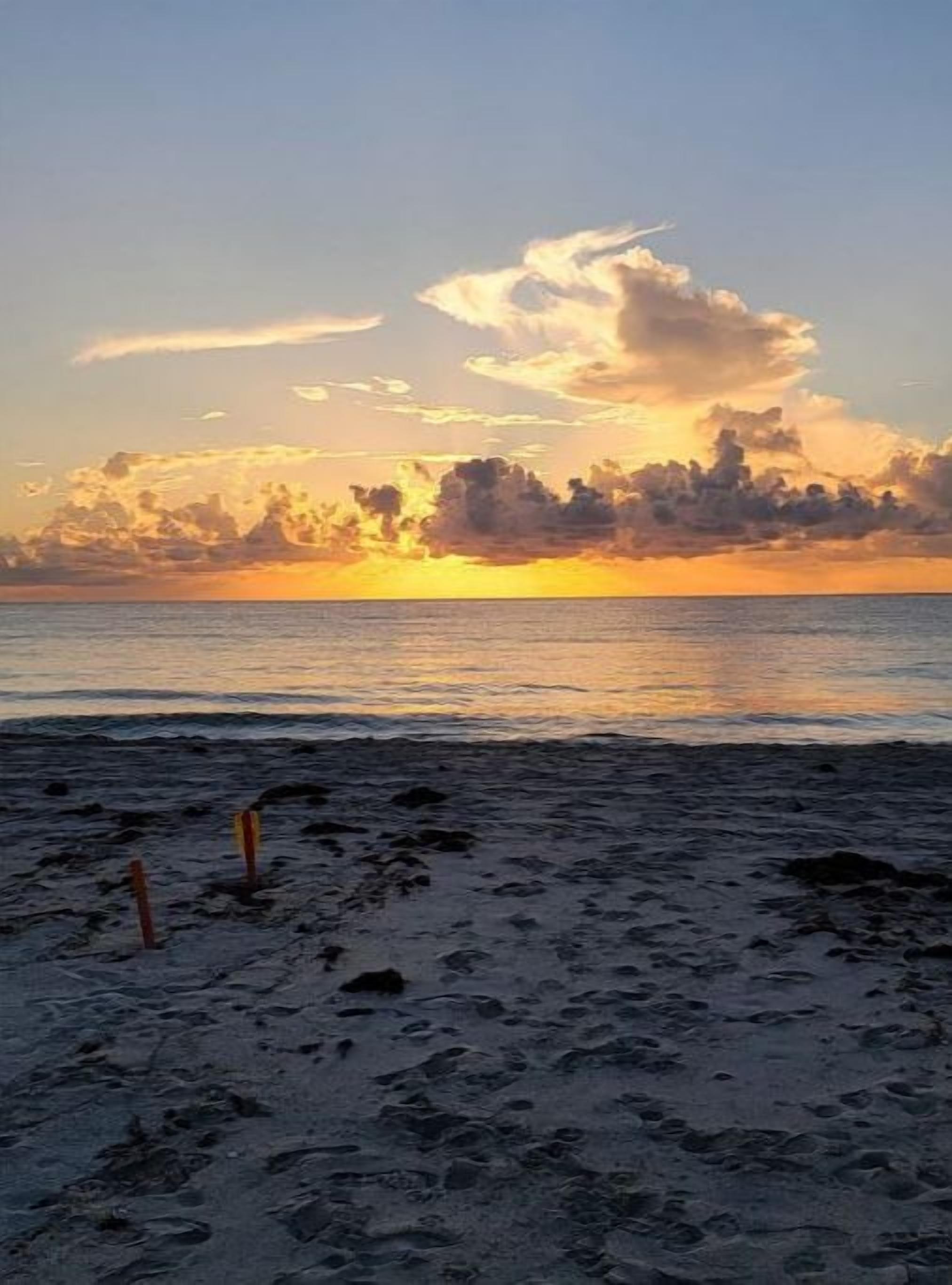 Een strand met voetafdrukken die naar het water leiden, een zonsondergang op de achtergrond en een bewolkte lucht.