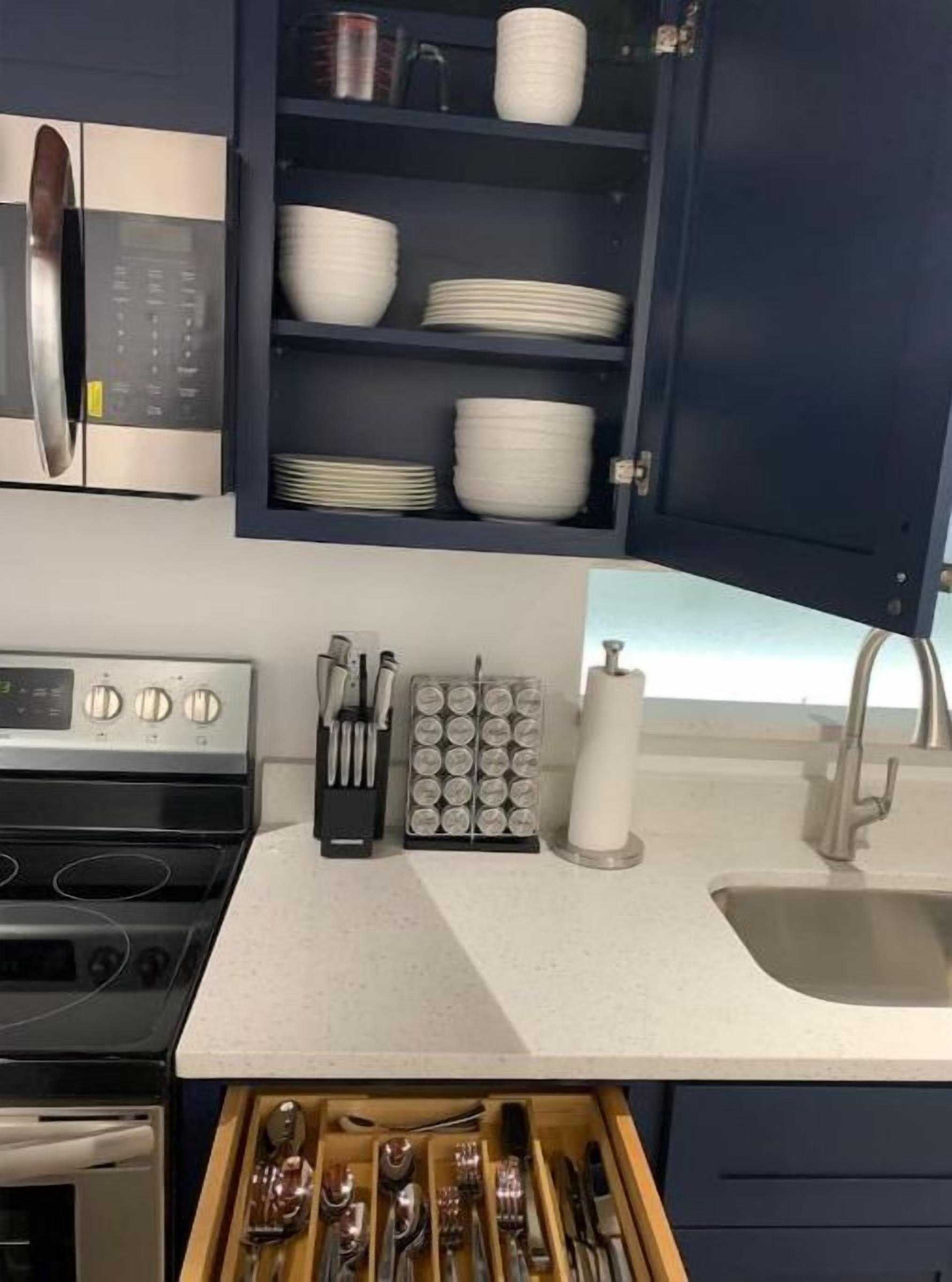 A kitchen with a microwave, stove, sink, and a drawer with utensils.