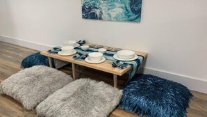 Ein Essbereich mit einem Holztisch, der für vier Personen gedeckt ist, mit zwei flauschigen Hocker, einem grau und einem blau.