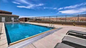 Una piscina sotto un cielo azzurro limpido, con un'area recintata e un edificio sullo sfondo.