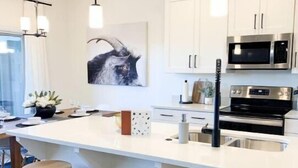 Una cucina moderna con mobili bianchi, elettrodomestici in acciaio inossidabile e sgabelli di legno.