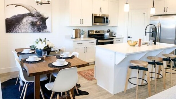 Una cucina moderna con mobili bianchi, elettrodomestici in acciaio inossidabile e un'isola centrale con sgabelli da bar.