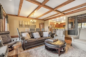 A spacious living room with a leather sofa, a round coffee table, and a chandelier.