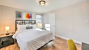 A bedroom with a large bed, a nightstand with a lamp, a wall-mounted artwork, and a window. - Bay Shore Vacation Rental ~ 7 Mi to the Beach (Bay Shore)