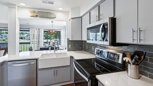 Una cocina moderna con armarios blancos, una estufa negra y vista a una casa a través del ventanal.