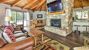 Una sala de estar acogedora con una chimenea de piedra, vigas de madera en el techo, un televisor grande y una zona de estar confortable.