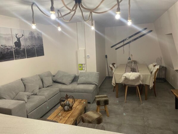 Uma sala de estar moderna com um sofá modular cinza, uma mesa de centro de madeira e um espaço de jantar com mesa e cadeiras.