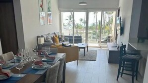 Un vaste espace de vie comprenant une table à manger dressée pour le repas, un canapé et un téléviseur fixé au mur.