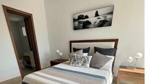 Une chambre à coucher avec un lit, une table de chevet, une commode et un tableau accroché au mur.