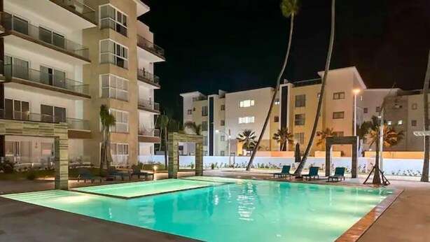 Une piscine entourée de bâtiments à plusieurs étages dotés de balcons, avec des chaises longues et des palmiers.