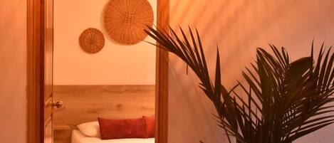 A hotel room with a bed, a potted plant, and a wall-mounted lamp.